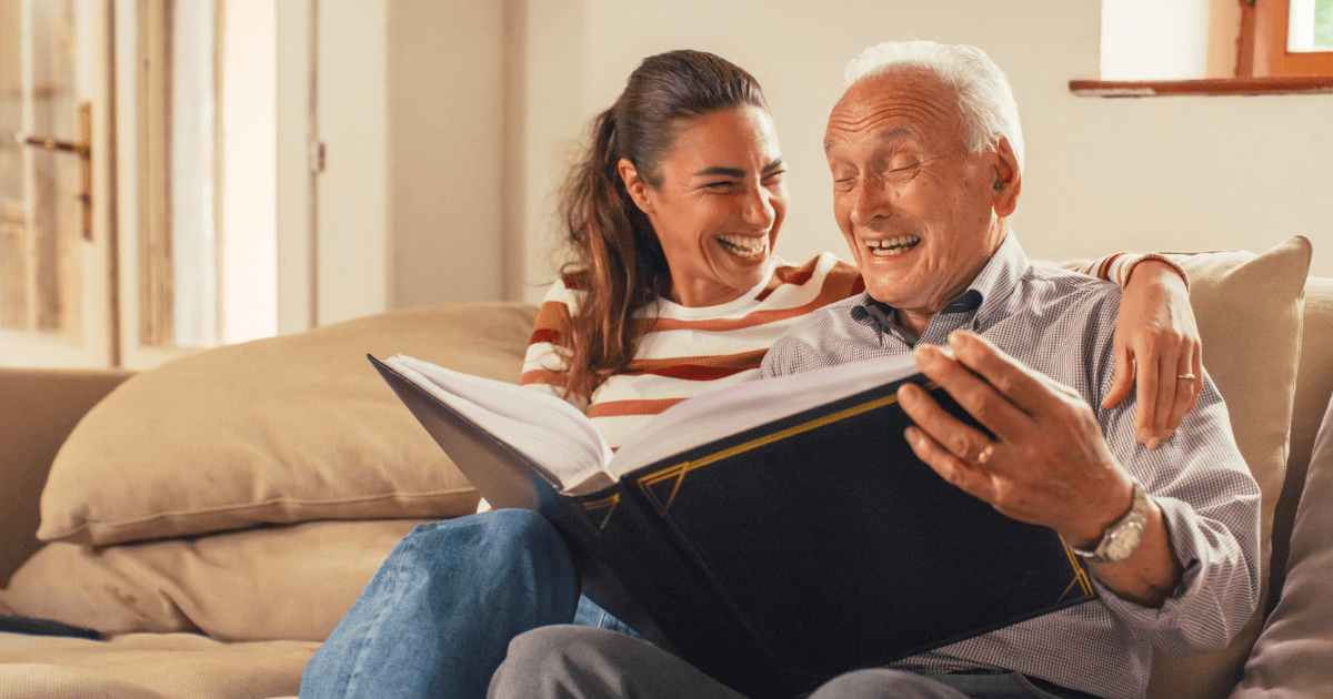 Young Granddaughter with arm around Grandfather memory care resident on sofa