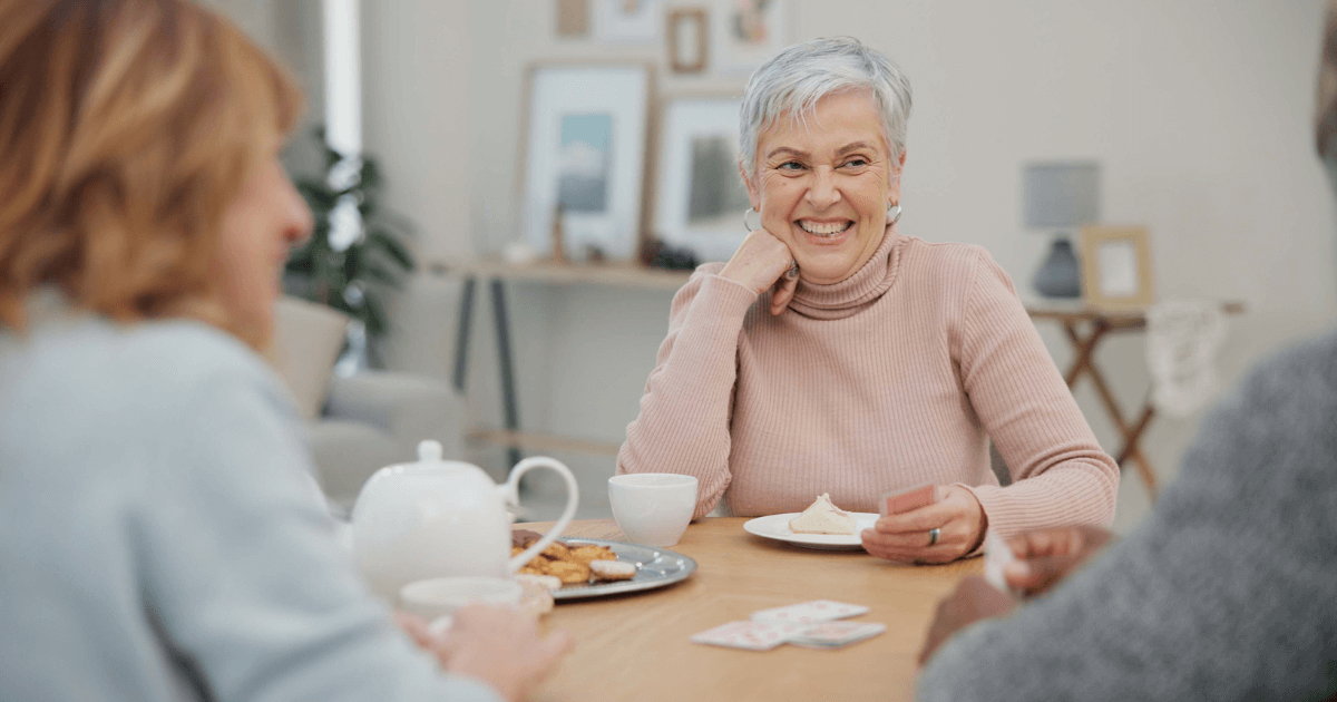 Group of seniors sitting at the dining table enjoying tea and cookies