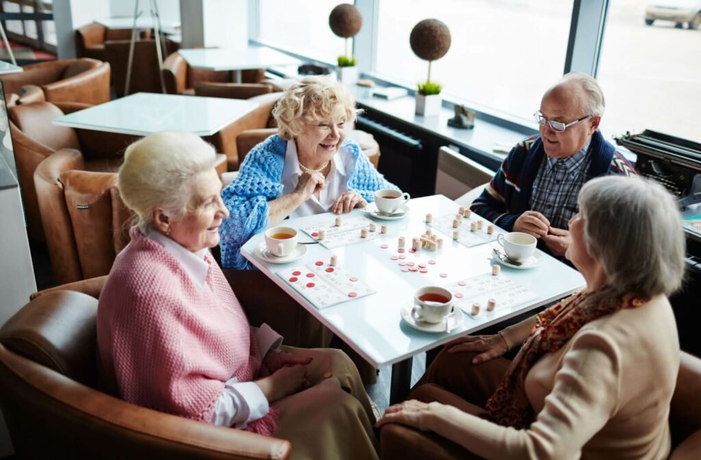 Group of happy seniors playing games and drinking tea around a square table.