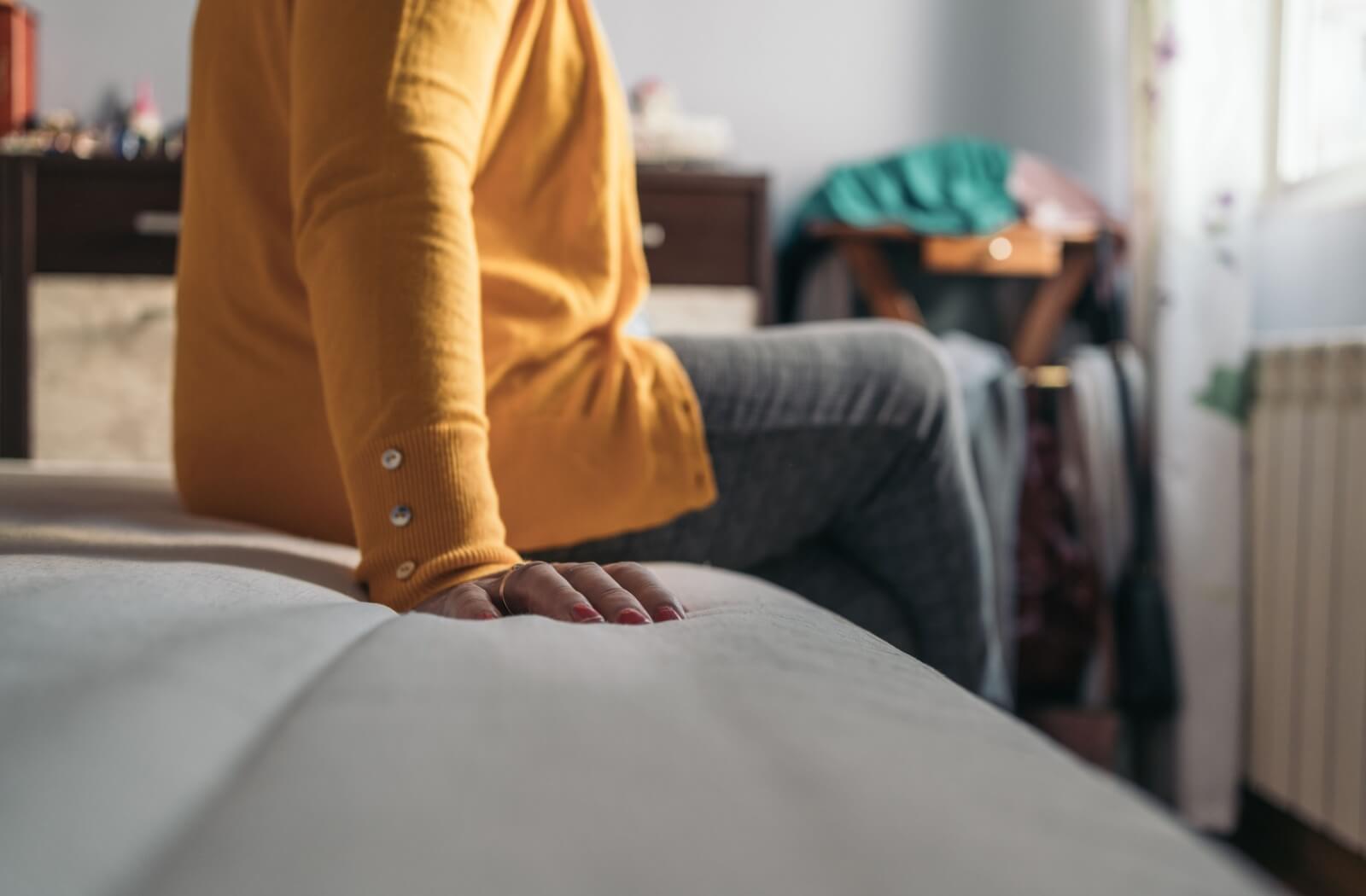 Close-up of a person’s hand as they sit on a bed in a cozy and sunlit room